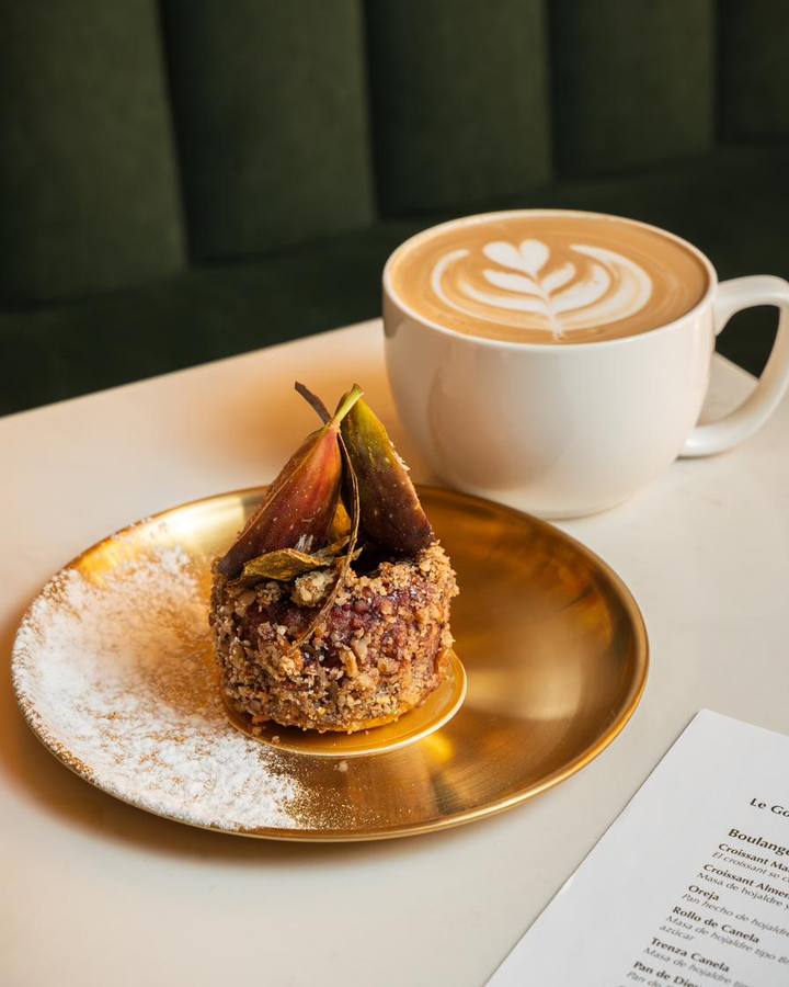 Latte con arte en la espuma junto a un pan dulce sobre plato dorado