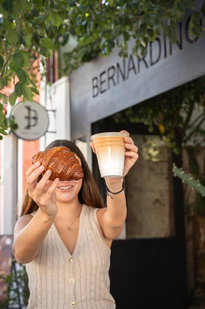 Visitante con un pan y un café frente al letrero de Bernardino
