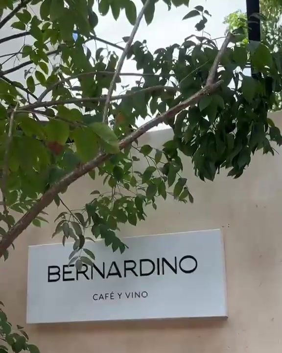 Letrero de Bernardino, café y vino, sobre el muro de la fachada bajo las ramas de un árbol
