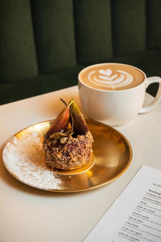 Latte con arte en la espuma junto a un pan dulce de higo sobre plato dorado