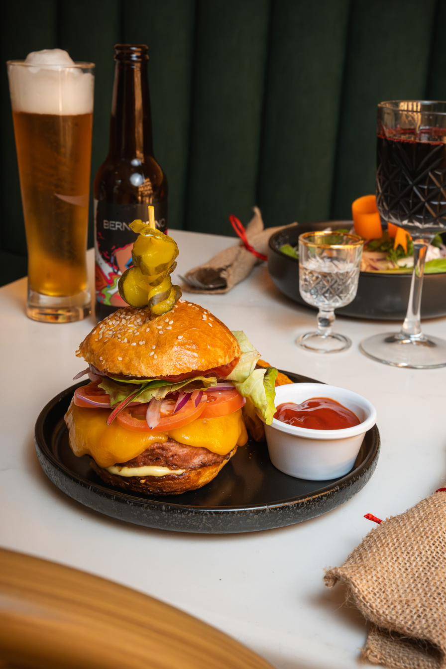 Una hamburguesa, cerveza y vino tinto en la misma mesa.