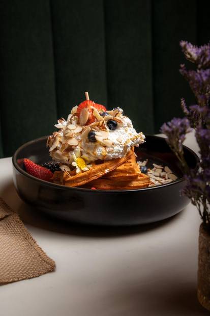 Plato de fruta y crema sobre mesa blanca con flores lilas
