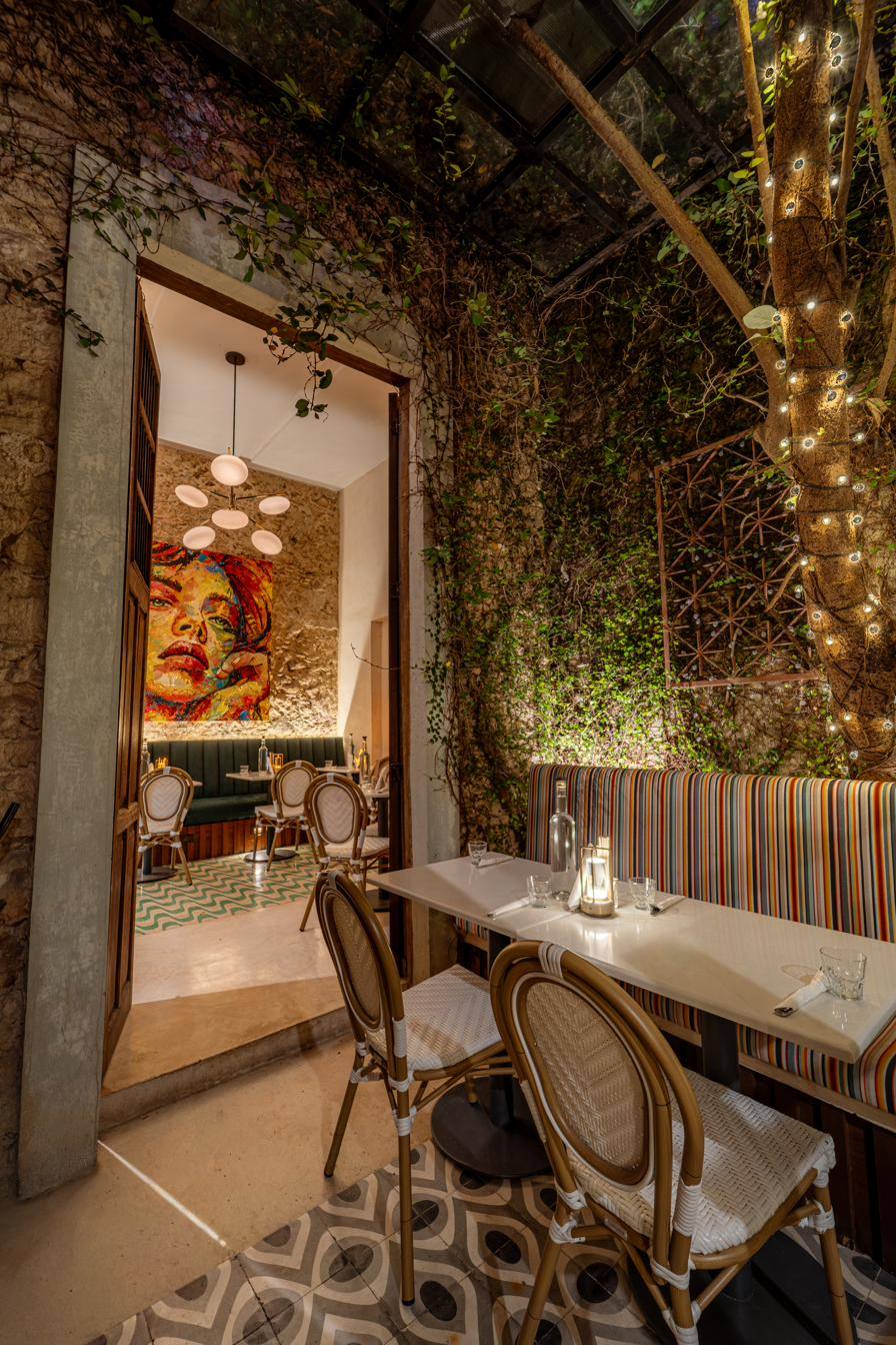 Entrada de piedra de Bernardino que se abre a un comedor con plantas, luces cálidas y un mural