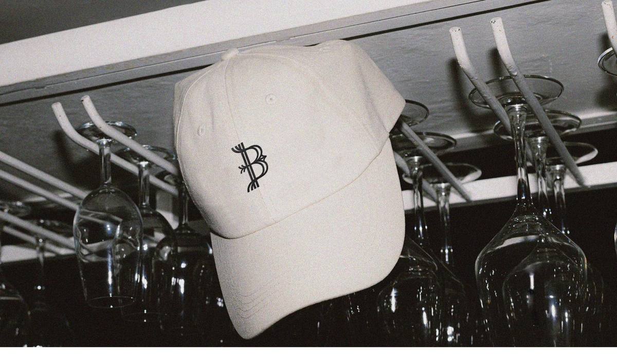 Gorra blanca con el monograma, entre copas.